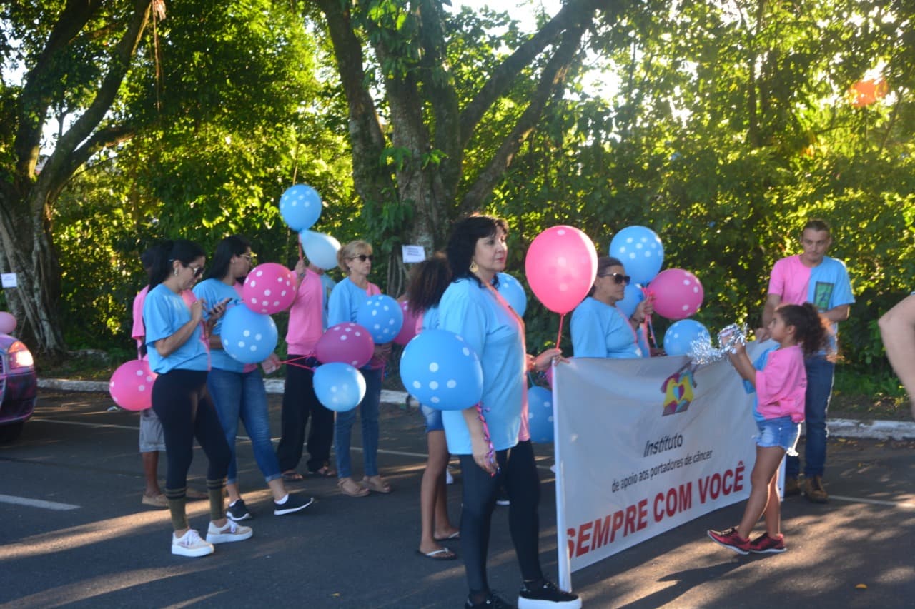 Faixa do Instituto do Câncer Sempre Com Você visível entre o público do desfile